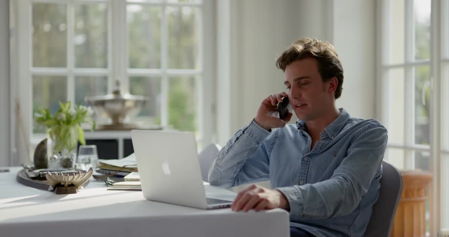 Man sitting at the table uses a laptop and answers the phone in the room