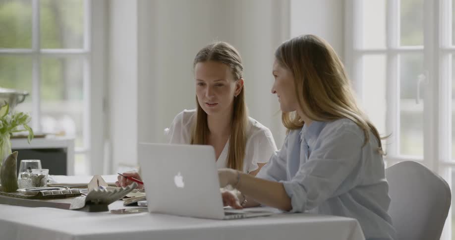 Two women work on a laptop and paper while discussing what is on the screen