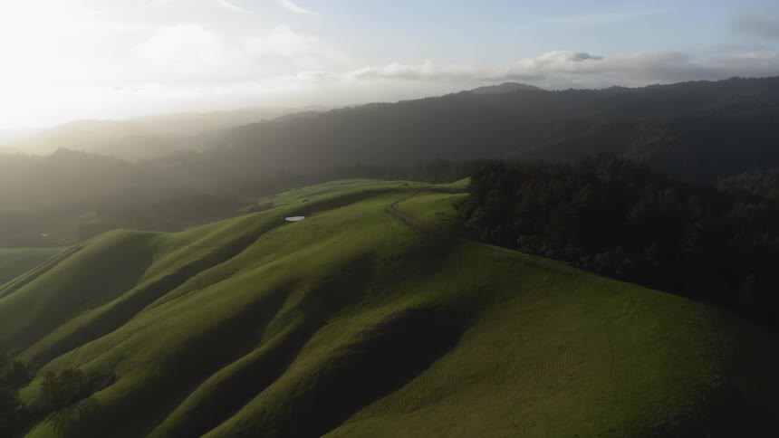 Smooth hills are covered in bright green grass as forests and mountains are seen in the distance