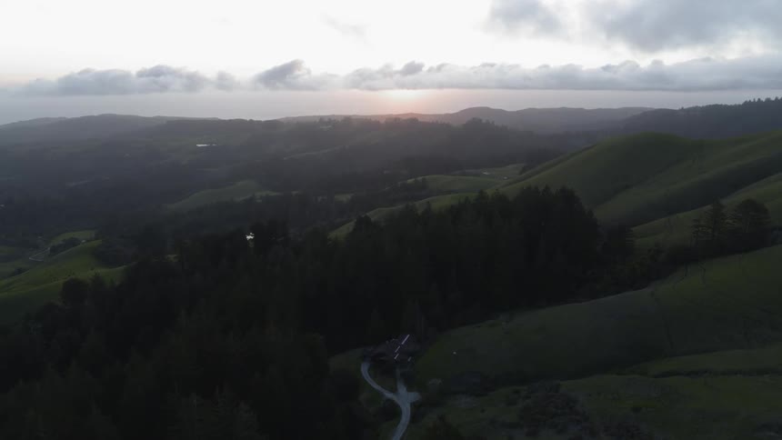 Sun rises over green hills dotted by forest