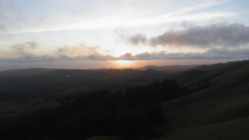 The sun sets on the horizon over green hills and slopes