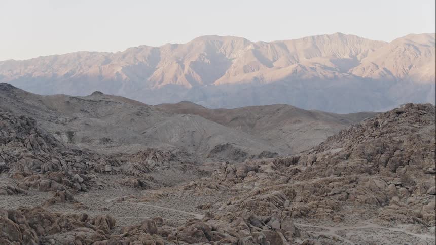 Dirt road winds around a rocky terrain with a ridge on the horizon