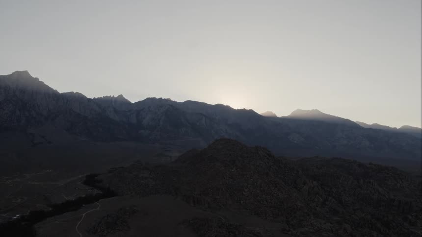 A view of barren mountain range in the far distance with hills at dusk