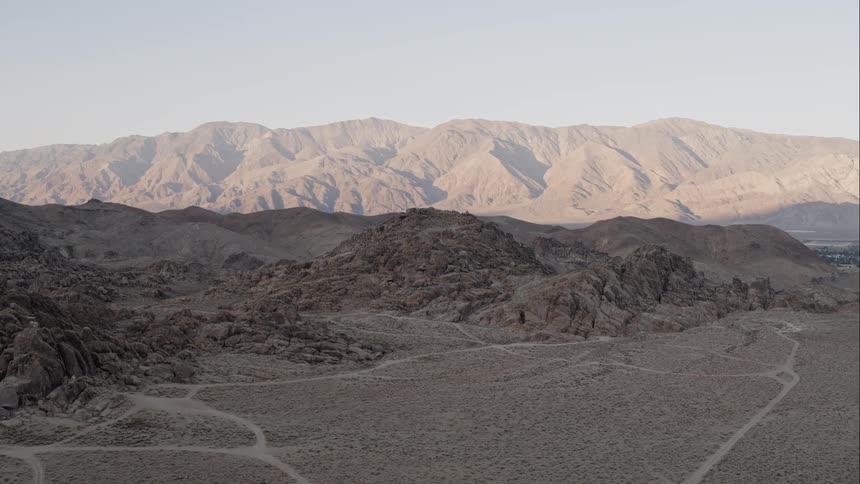 Dirt roads track a barren rocky terrain with a ridge on the horizon