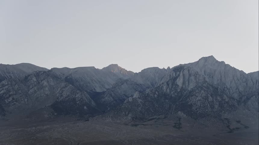A view of barren mountain range in the far distance with hills at dusk