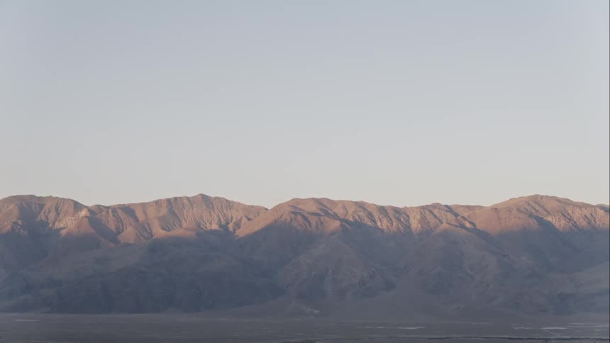 A mountain range with the sun shining on it and the sky in the background