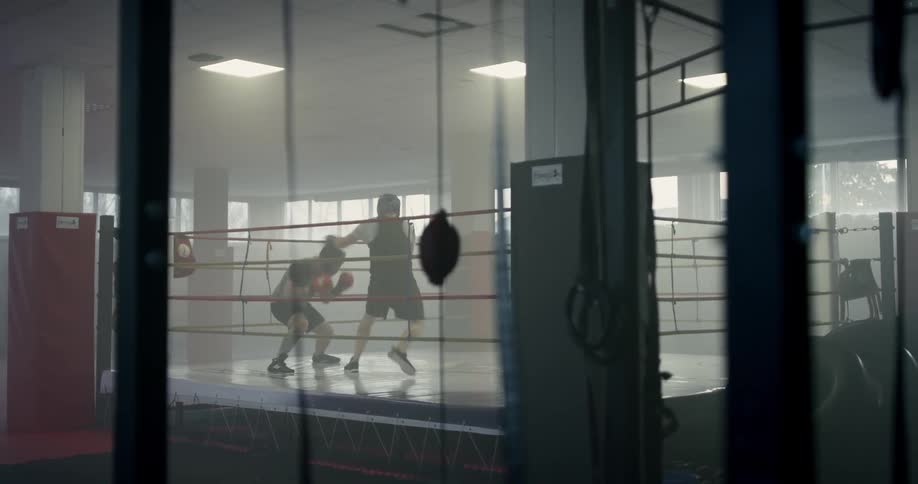 Two men spar in a boxing ring in a gym