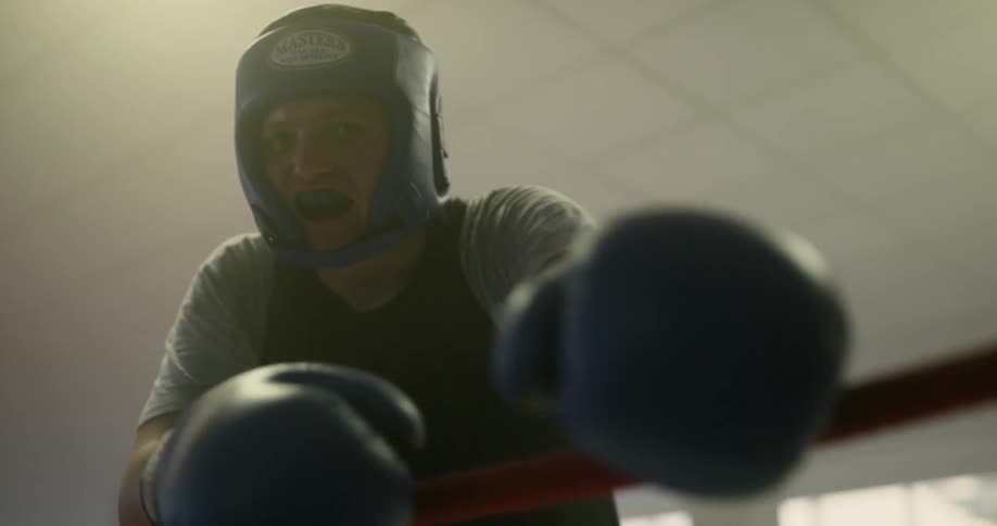 A boxer leans on the rope of a boxing ring