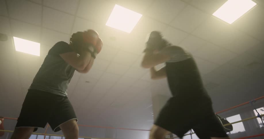 Boxers sparring on boxing ring inside gymnasium at sunset