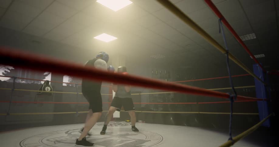 Two men wearing padded headgear exchange punches inside of a boxing ring as they spar
