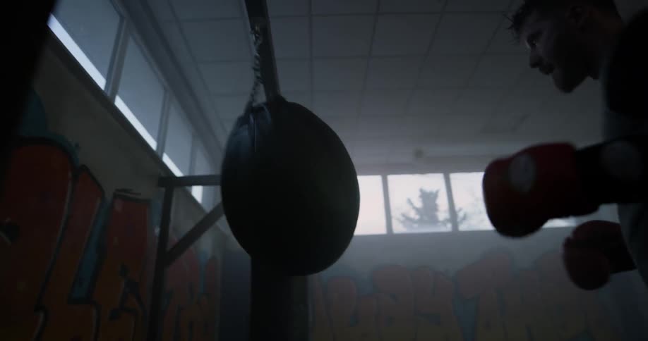 Male boxer punches heavy bag in the dark gym