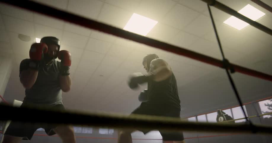 Two men spar in a boxing ring in a gym