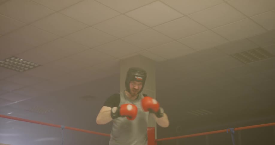 A man tightens his boxing gloves in a ring and pumps himself up
