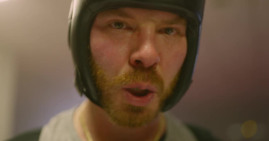 White man wearing boxing head guard shows the blue protective mouthguard in the boxing ring