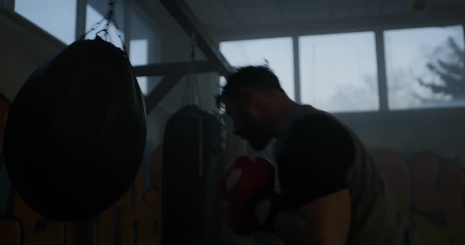 A man punches a rounded heavy bag in a gym with graffiti on the walls