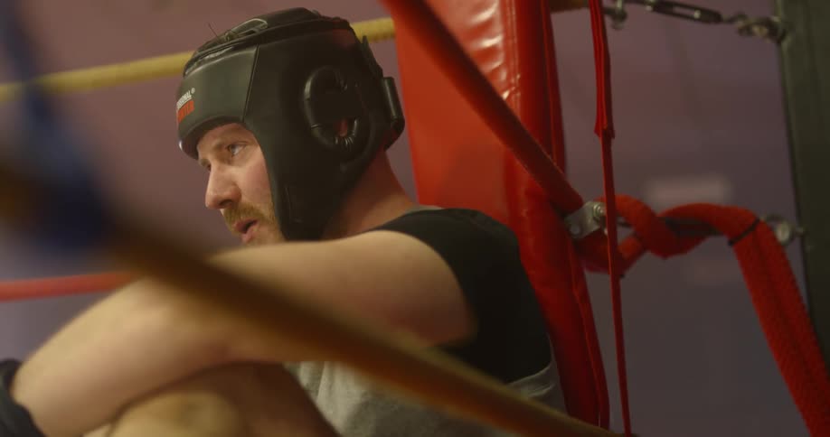 A boxer sits in the corner of a boxing ring exhausted