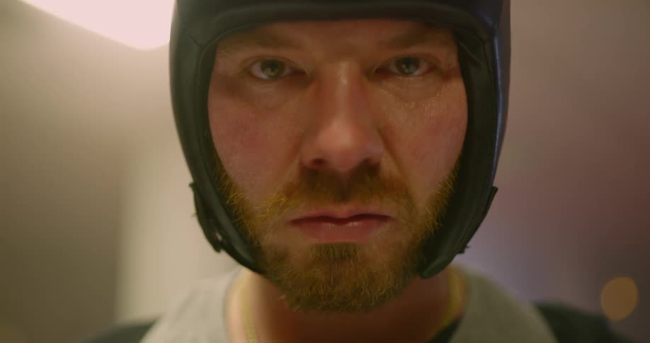 Male boxer wearing a head guard looks at the camera angrily in the boxing ring