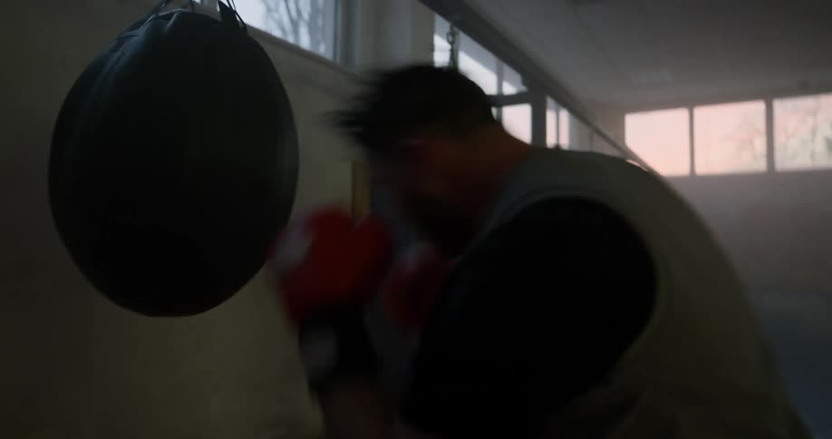 A white male is wearing boxing gloves to punch a punching bag in a gym