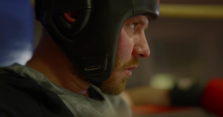 A man wearing fighting pads and headgear catching his breath