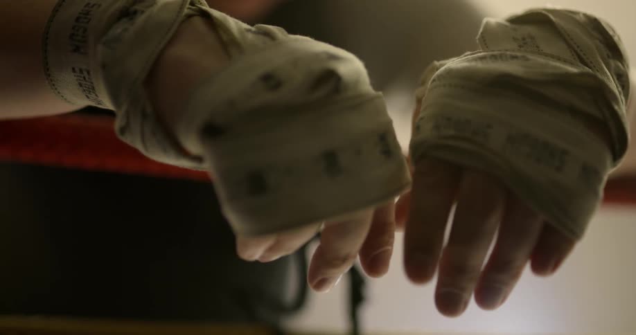 A boxer with hands taped rests on the ropes after a match