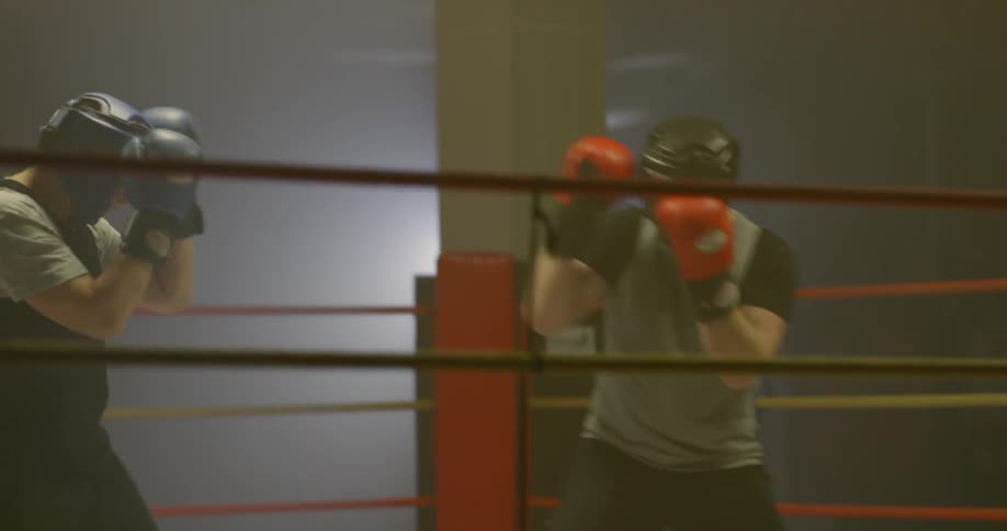 Two men wearing protective gear spar in the boxing ring