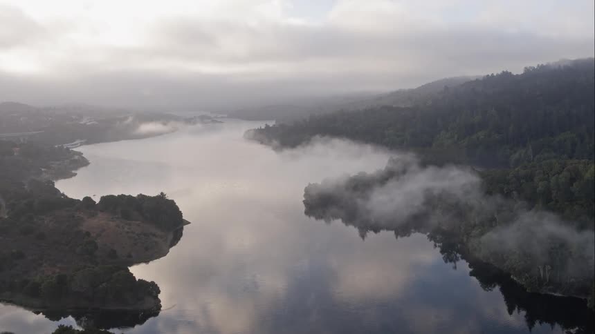 A large body of tranquil water is lined by heavily forested hills