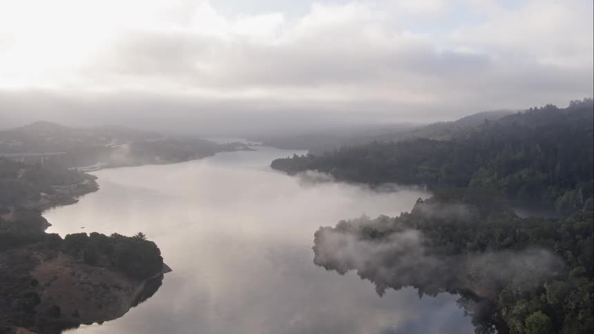 A large lake is bordered by forest covered hills on a cloudy day