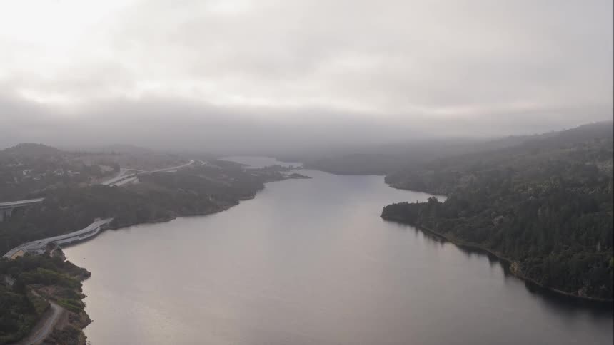 A large river flows through a foggy forested area next to a number of roadways