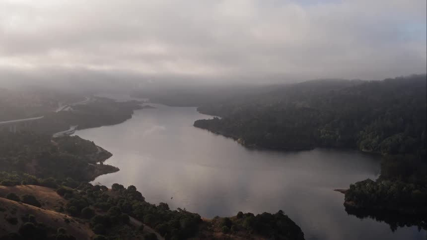 A river through a hills covered in forest on a cloudy day