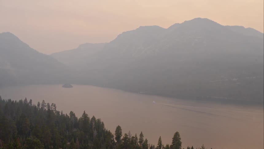 A boat in a mountain lake leaves a wake at sunset