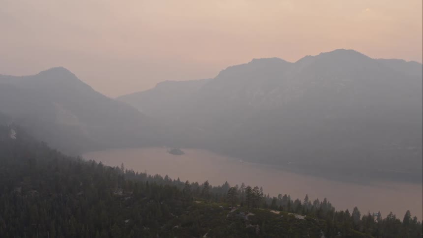 A mountain lake surrounded by slopes and forest trees on a foggy morning
