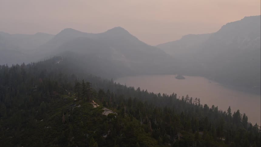 Tree covered slope lead down to a mountain lake at sunset