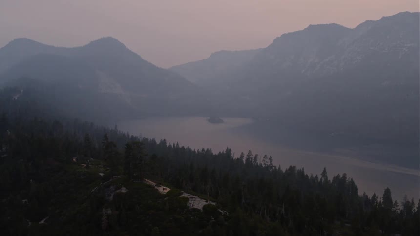 A boat leaves a wake in a mountain lake surrounded by forest trees and sloping hills