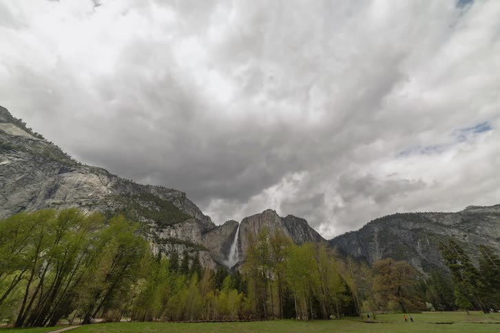 Clouds pass over a ridge with a rushing waterfall and paths with tourists