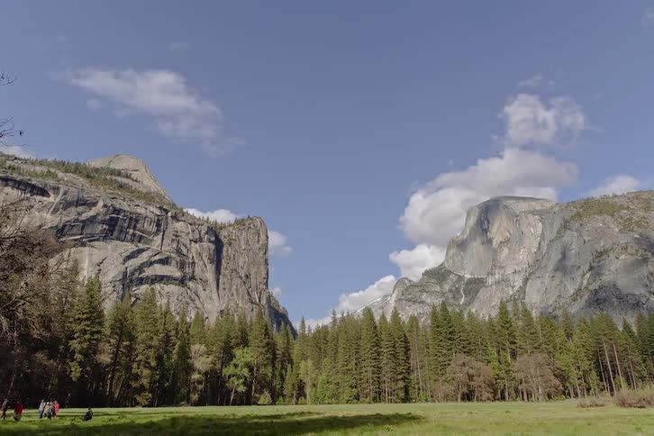People walking on a field with trees and cliffs in the background