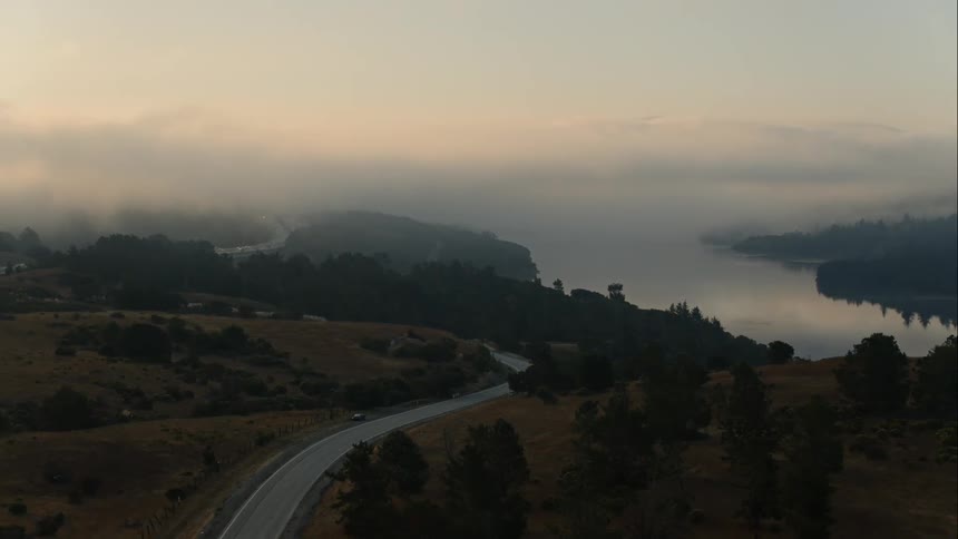 A road winds through a hilly landscape off the coast of the ocean