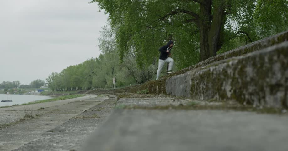 A man is running on a paved path next to a lake and then runs up a few cement steps to a path at a higher elevation