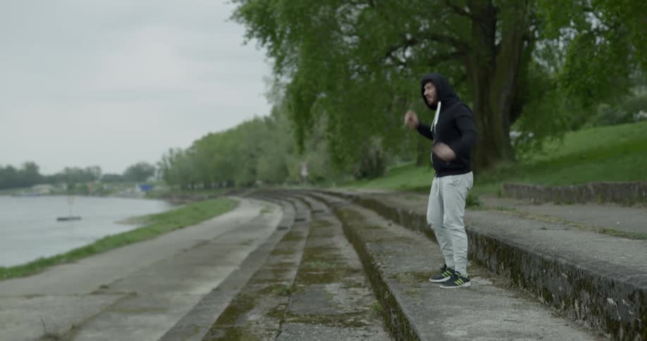 A man ties his sneaker then puts up his hood as he stretches and warms up for a run