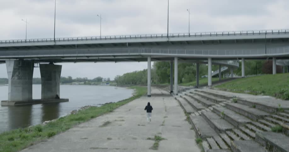 Man runs along the road next to the river under the bridge on a cloudy day