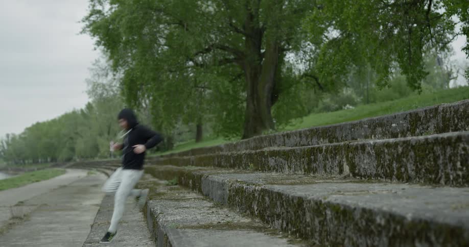 A man is running up and down wide cement steps at a park with a large weeping willow tree in the background and a lake off to the side