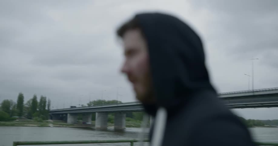 A man stands near the water with his hands on his hips and looks around