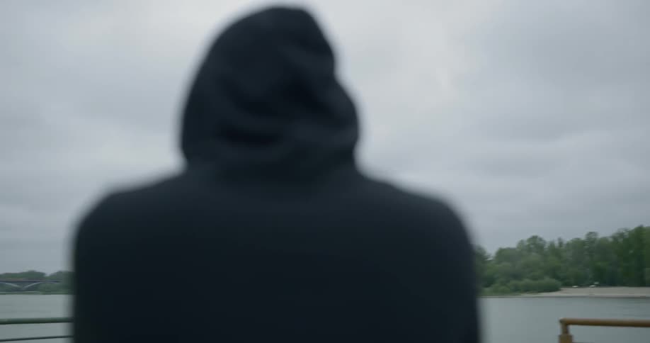 Man in black hoodie looks at the river on a cloudy day
