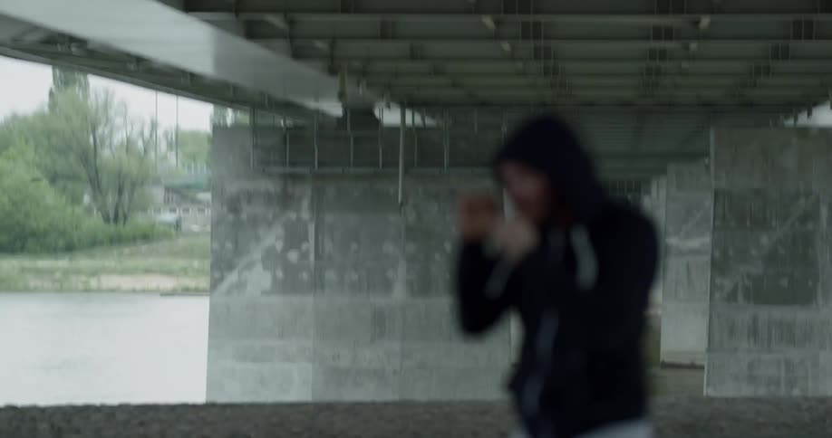 Man in black hoodie practices punching and trains alone under the bridge