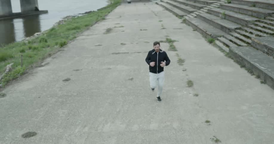 Man in black hoodie runs along the road next to the river on a cloudy day