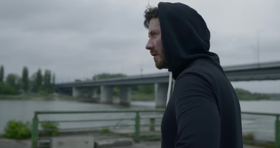 A man wearing a sweatshirt stands beside a waterway