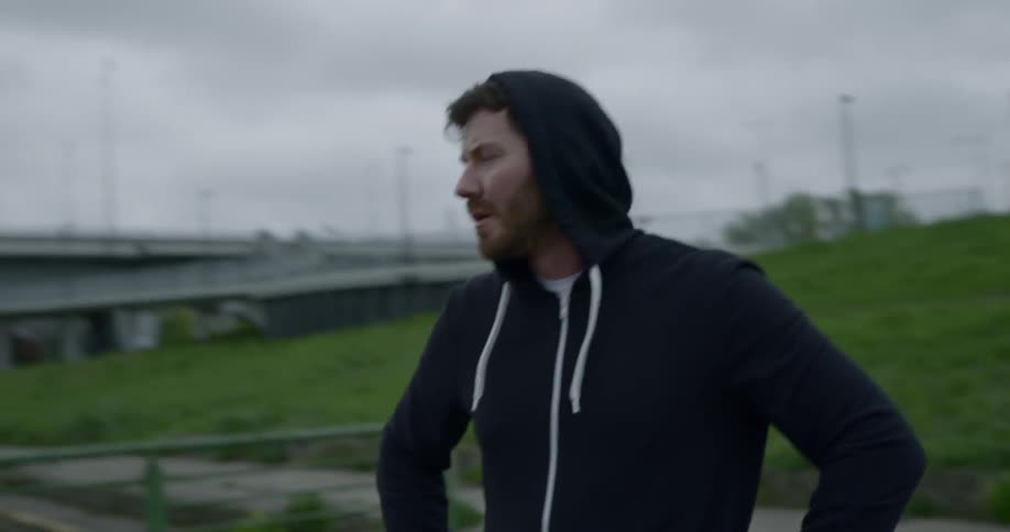 A man in a hoodie with hands on hips looks around the reservoir on a cloudy day