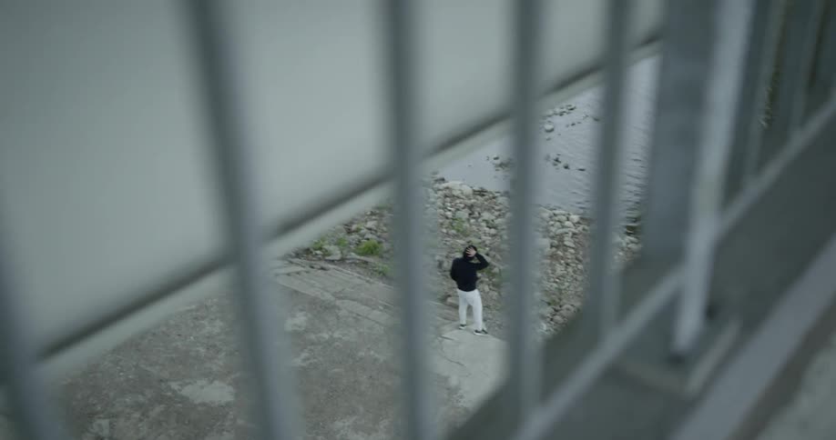 Man wearing a black hoodie stands next to the river under the bridge on a cloudy day
