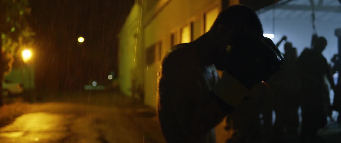 A man is tapping his head wearing boxing gloves as it rains at night