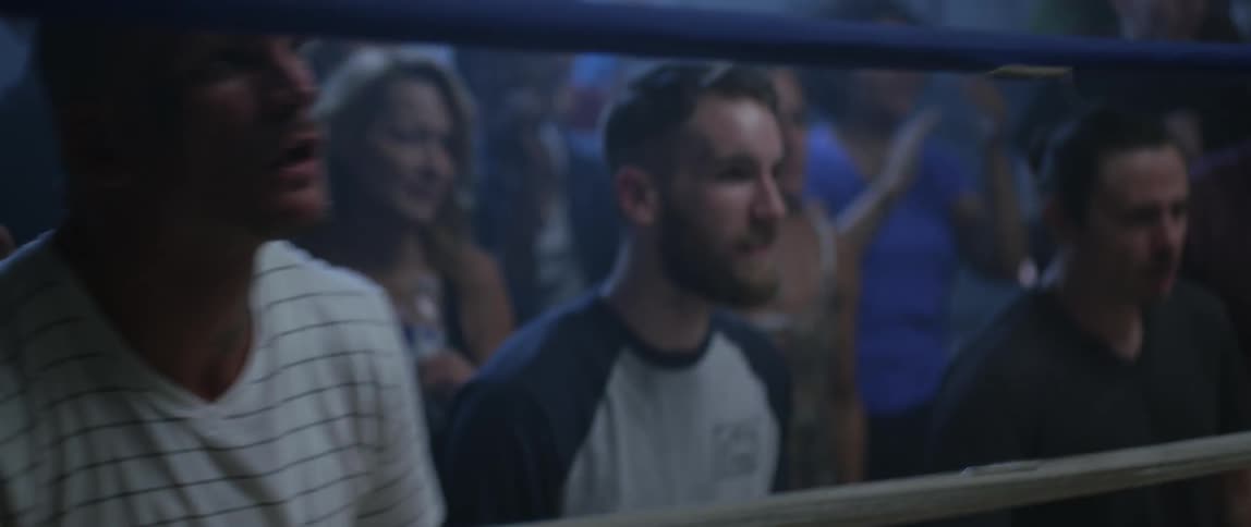 People cheer by the side of a ring as a fighter raises his arms