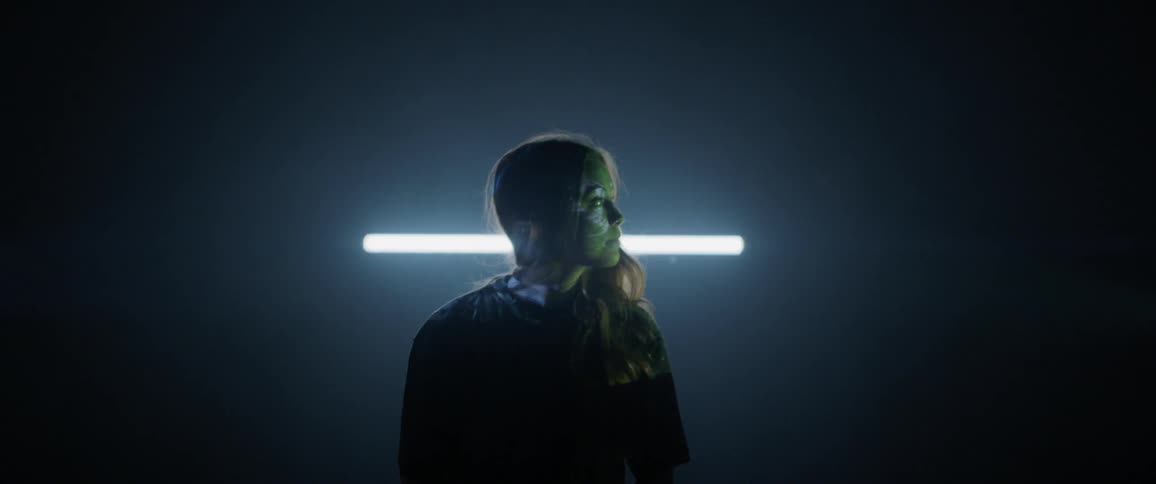 A woman sits in a dark room with light projecting patterns onto her face and body